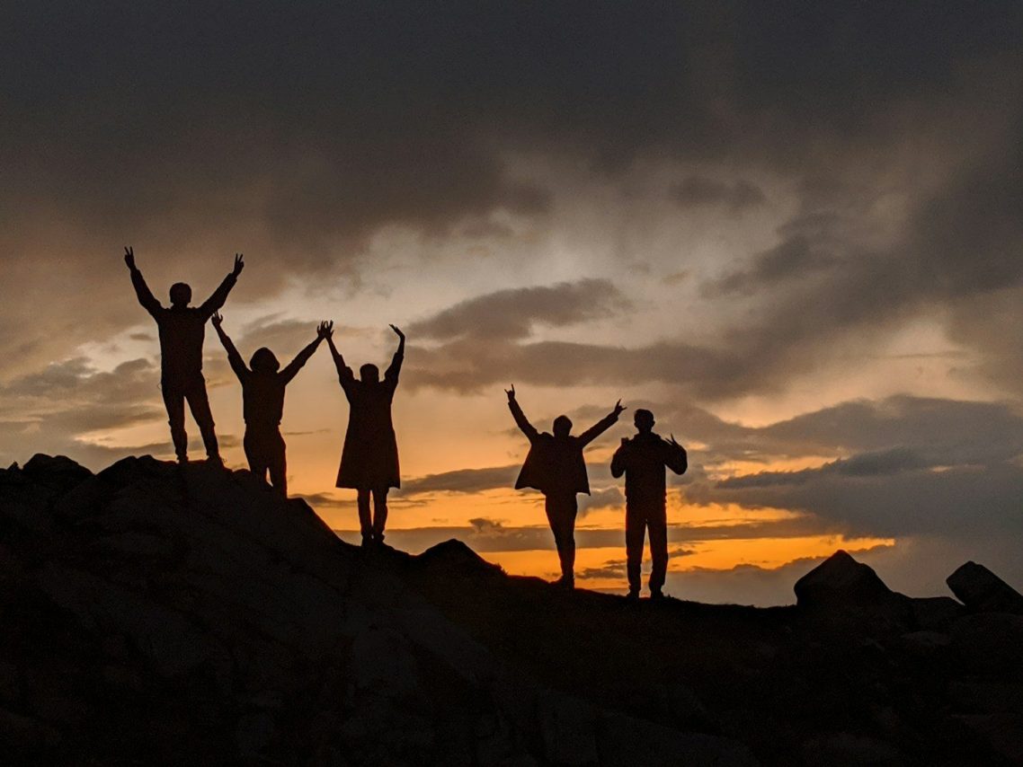 Silhouettes of five people on a rocky landscape against a colorful sunset sky.