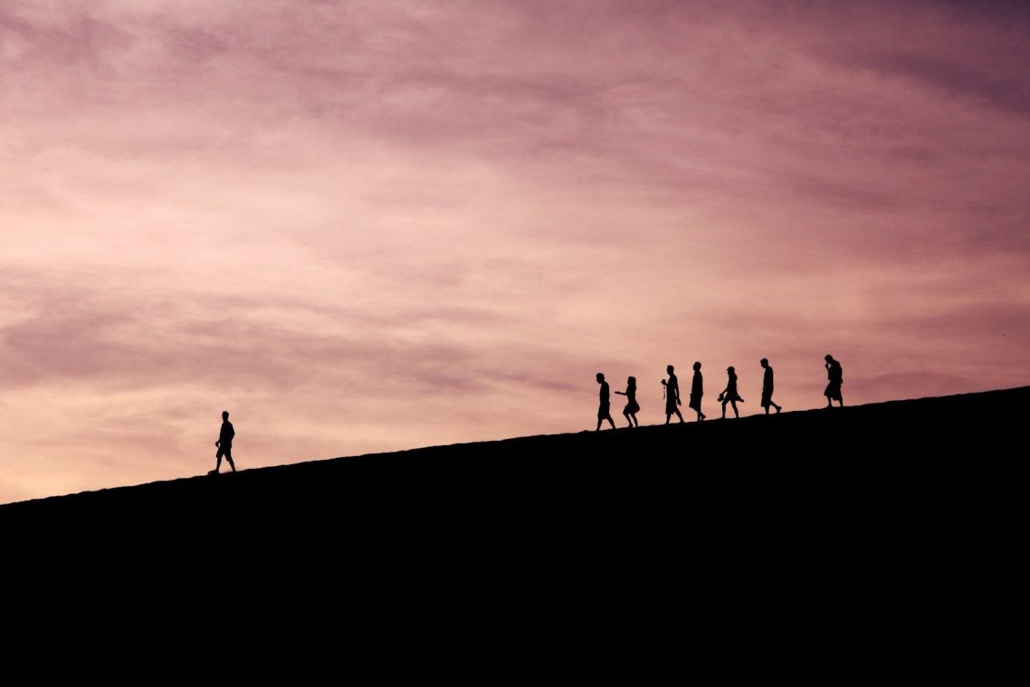 Silhouettes of people walking on a hill at dusk, with a purple sky.